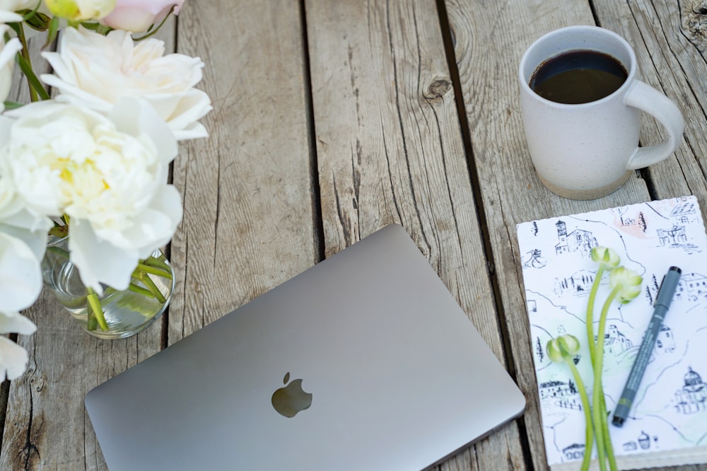 silver macbook beside white ceramic mug on brown wooden table