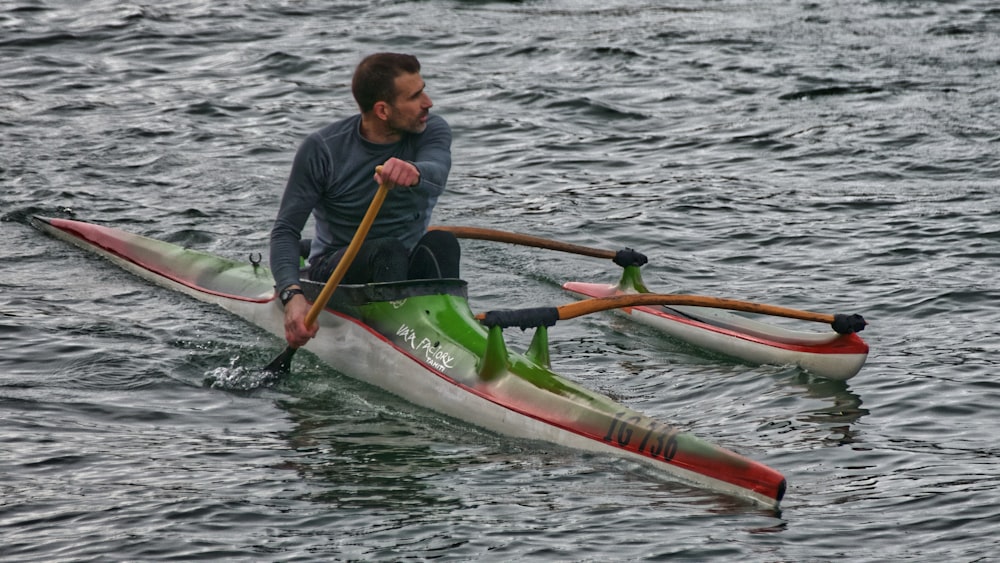 uomo in giacca nera che cavalca su kayak verde e giallo sullo specchio d'acqua durante il giorno