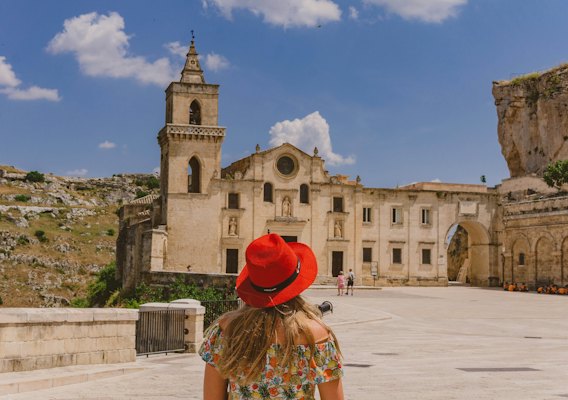 Woman in red hat standing near brown concrete building during daytime — Matera, Italy