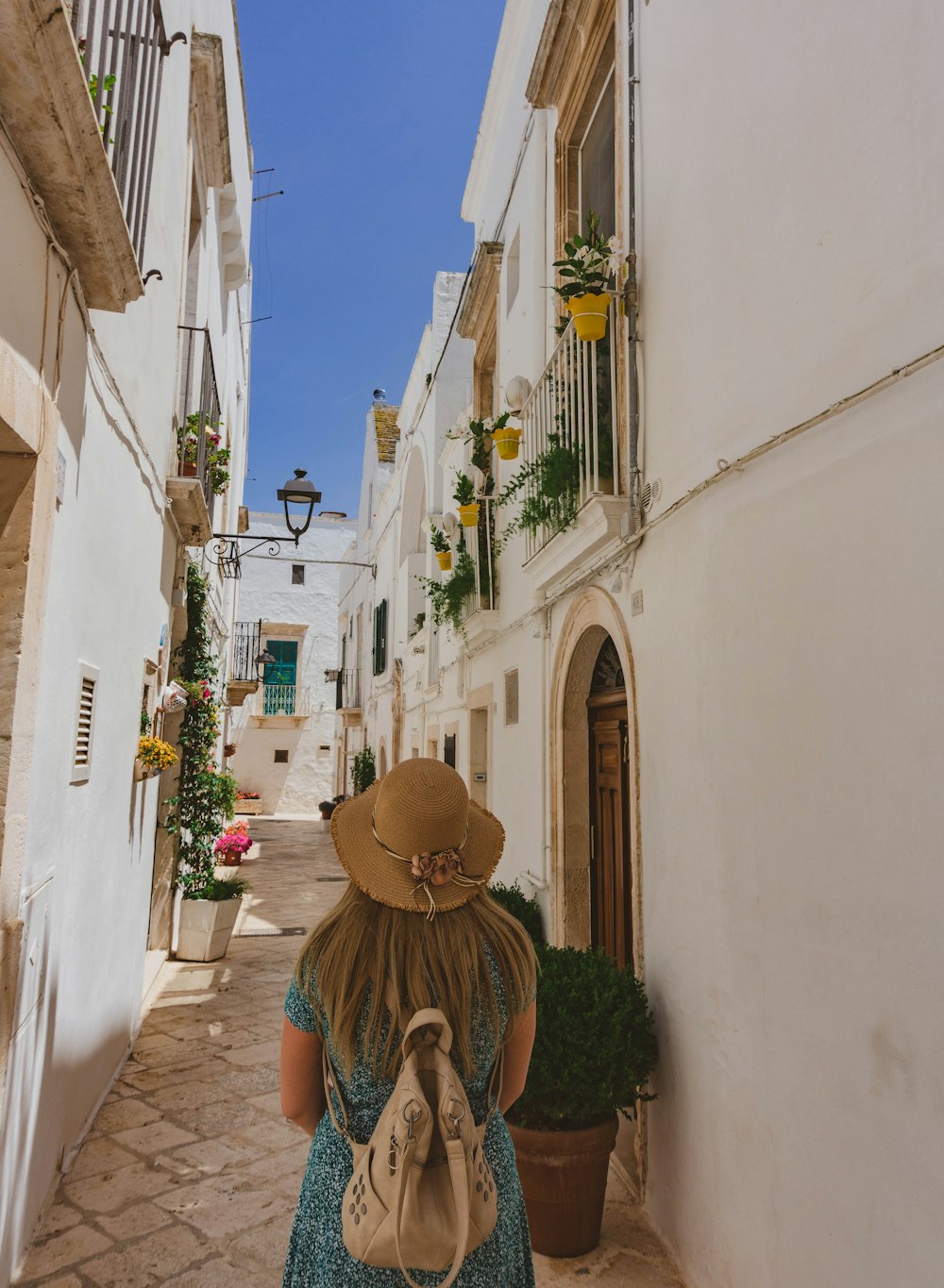 woman in brown hat standing in between white concrete buildings during daytime