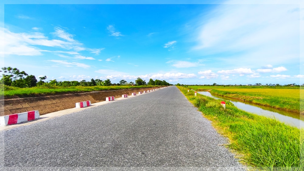 gray concrete road between green grass field under blue sky during daytime