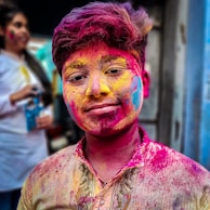 woman in purple and brown floral button up shirt with pink and blue powder on face