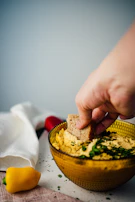 A child happily dipping carrot sticks into a small bowl of creamy hummus.