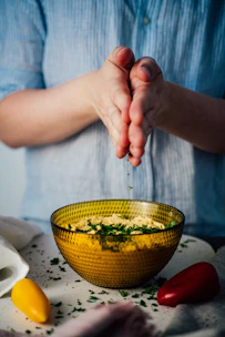 Artisan hands sprinkling a fragrant seasoning mix over fresh vegetables on a natural wood surface.