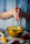 A joyful person sprinkling biryani masala over a steaming pot, kitchen background with brass utensils and clay pots.