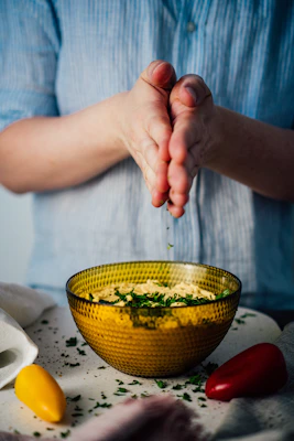 Artisan hands sprinkling a fragrant seasoning mix over fresh vegetables on a natural wood surface.