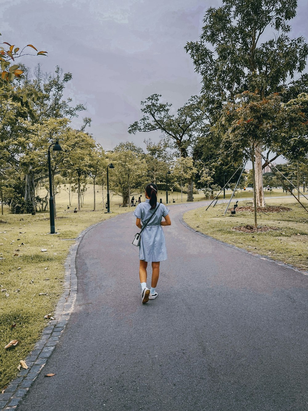 Mujer con chaqueta de mezclilla azul caminando por la carretera de asfalto gris durante el día