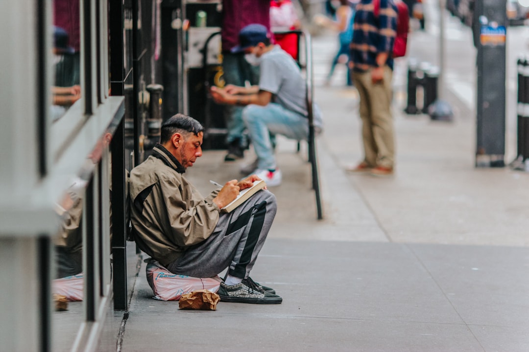 man in brown jacket sitting on sidewalk during daytime