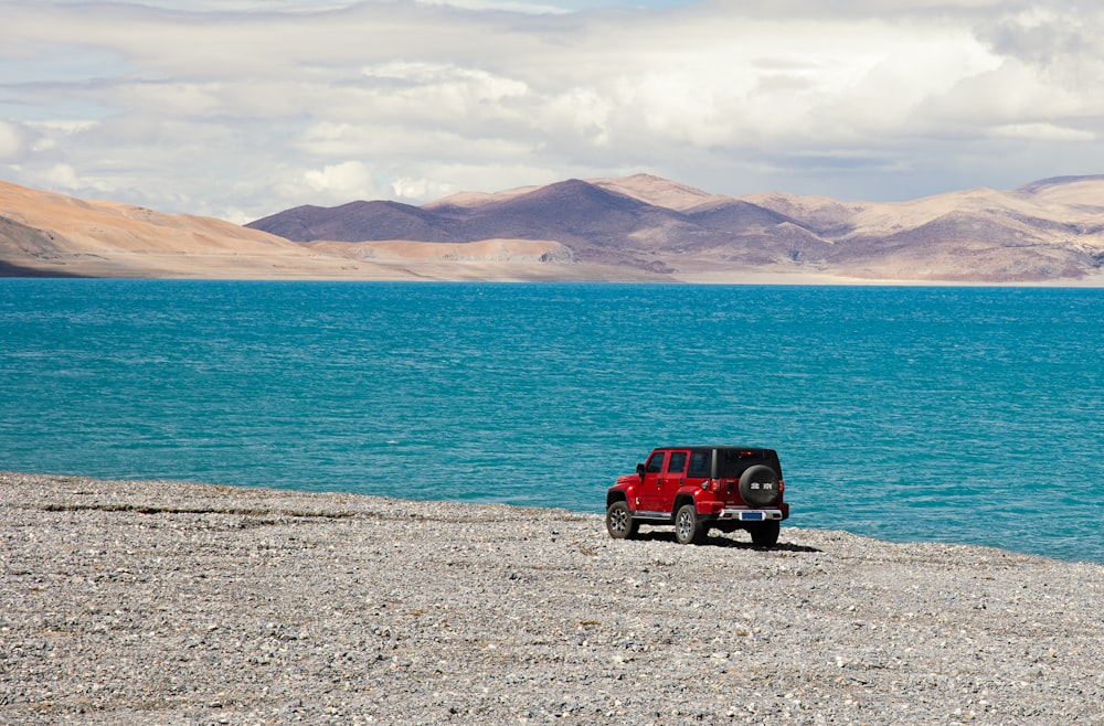 red and black jeep wrangler parked near body of water during daytime
