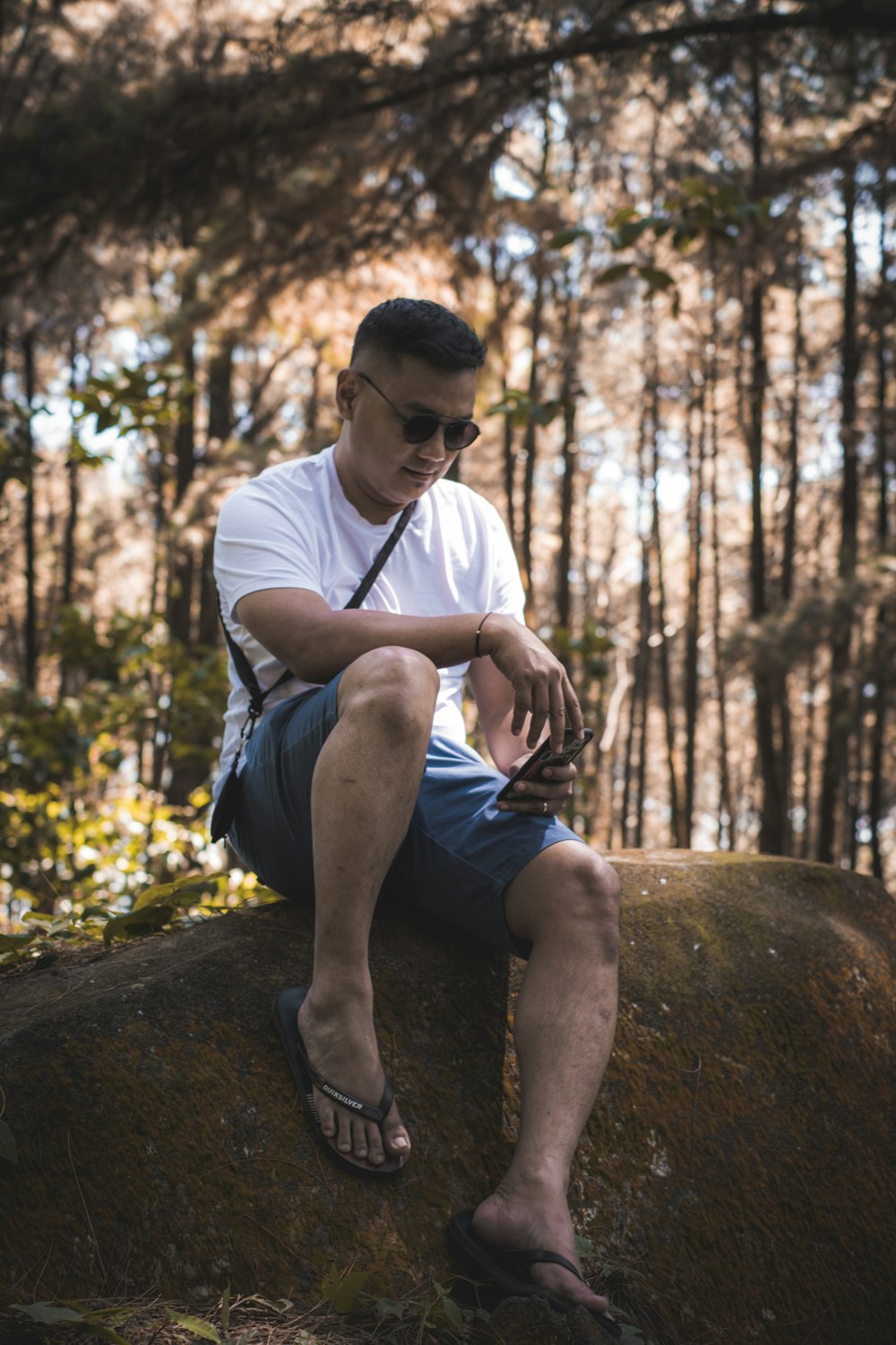 man in white t-shirt and blue denim shorts sitting on tree log during daytime