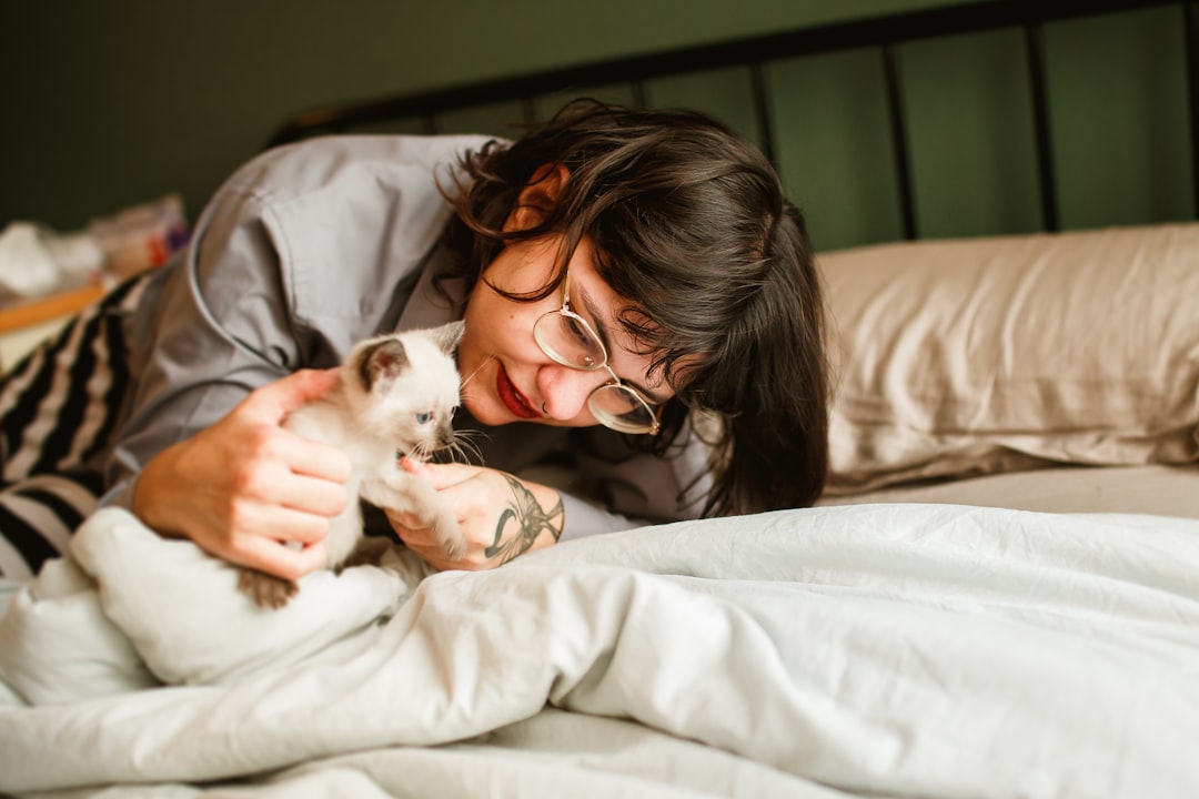 woman in black framed eyeglasses kissing white cat on bed