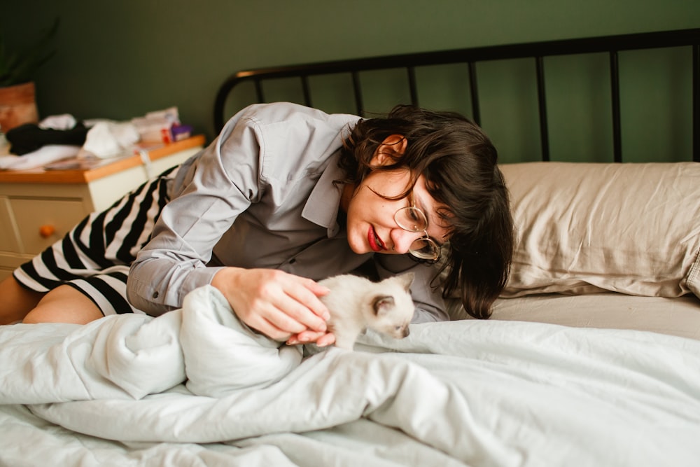 woman in gray long sleeve shirt lying on bed with white cat