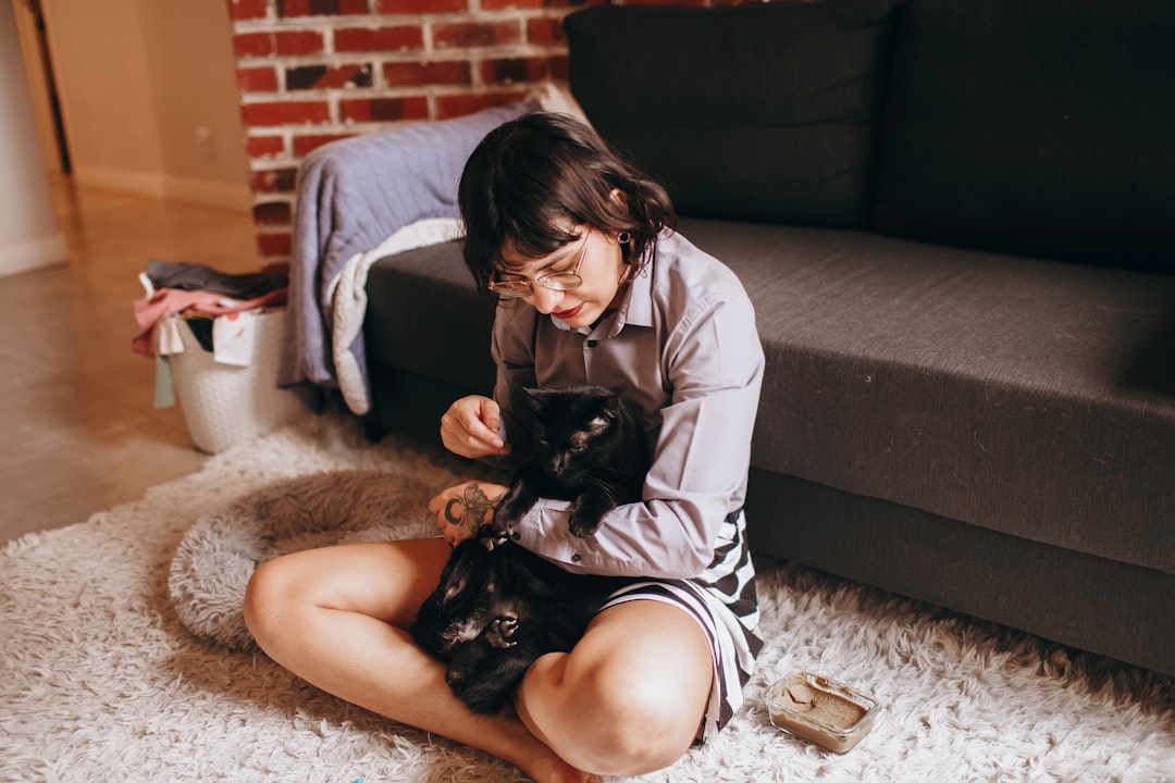 woman in white shirt and black shorts sitting on floor beside black cat