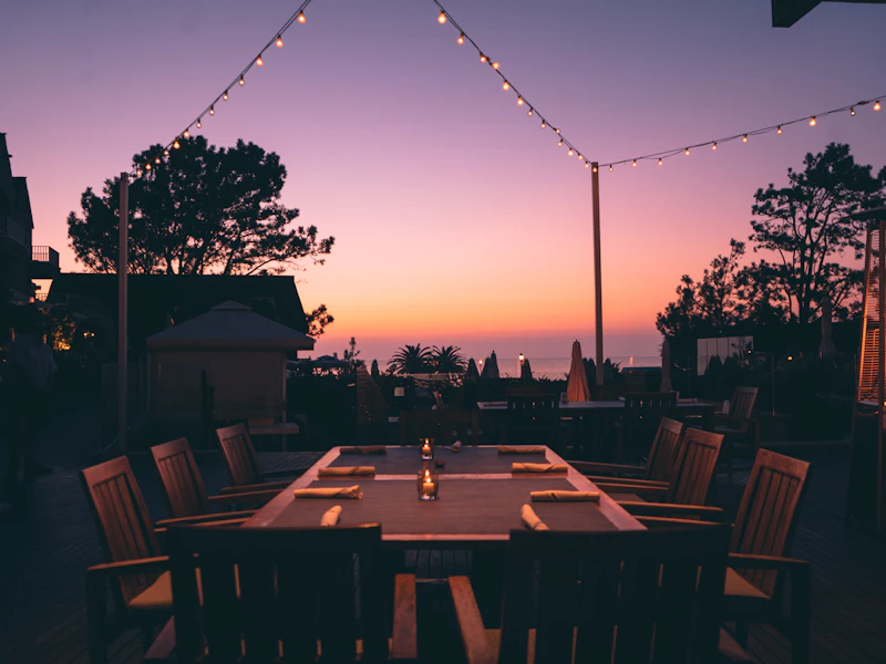 A dinner table set on the terrace under string lights at dusk