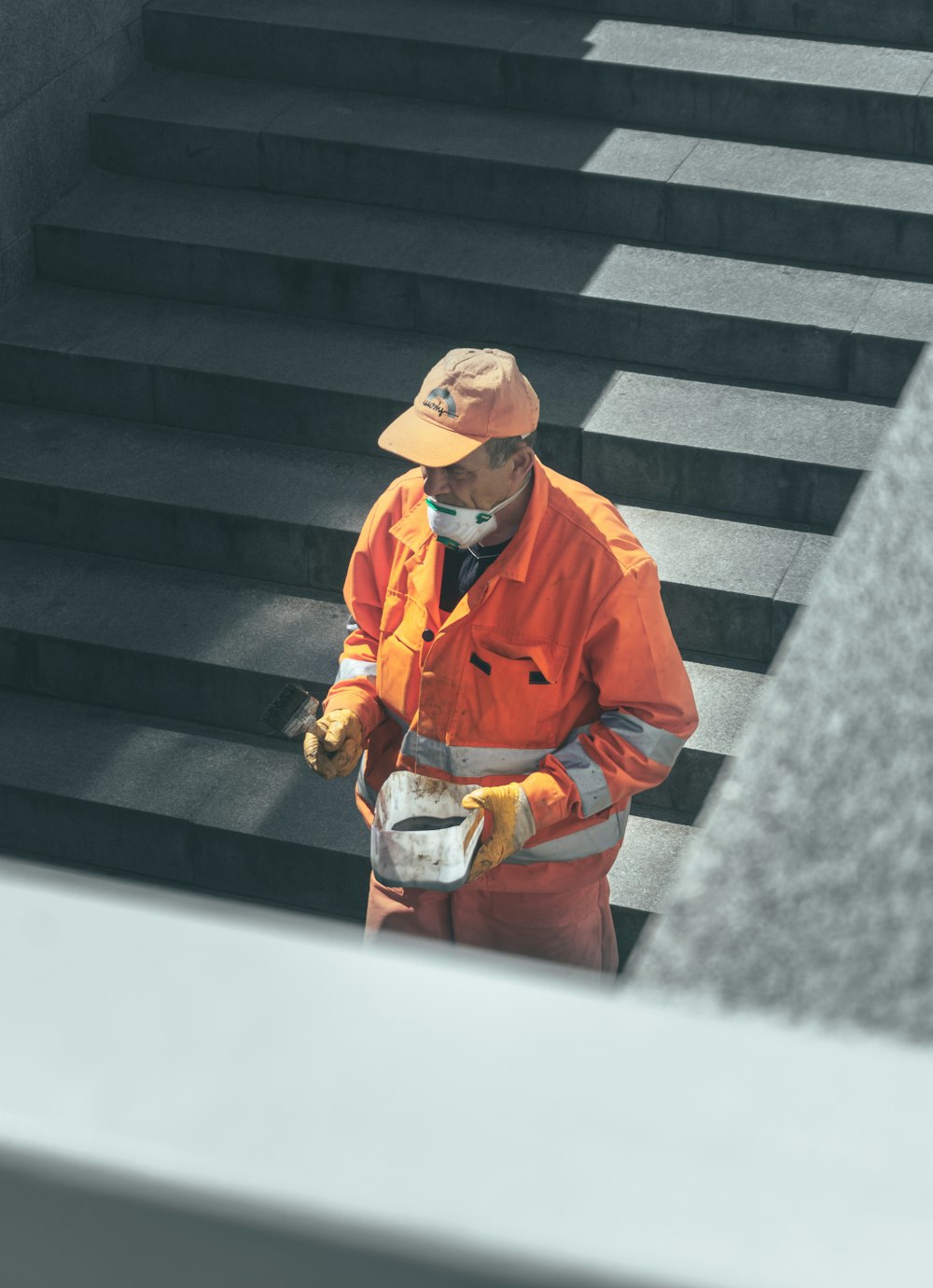 man in orange jacket and brown hat standing on gray concrete stairs