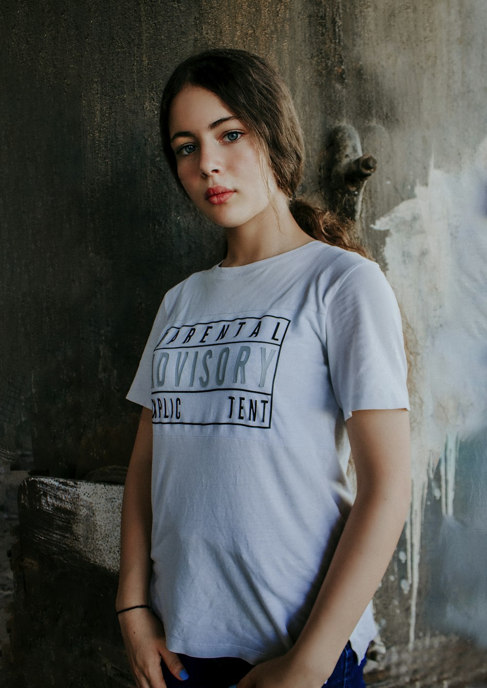 Mujer con camiseta blanca de cuello redondo de pie junto a una pared de hormigón gris