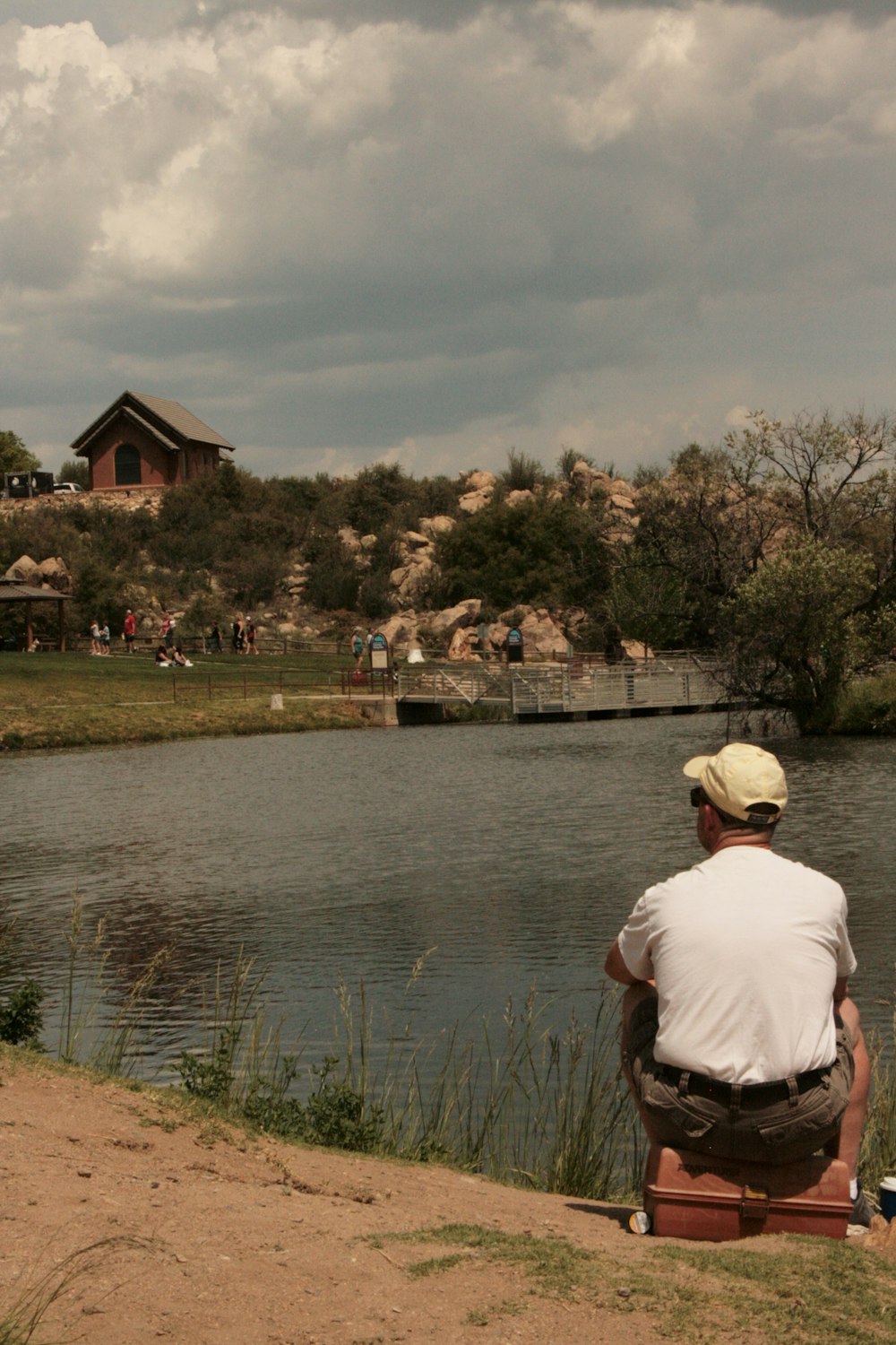 man in white shirt sitting on grass field near body of water during daytime