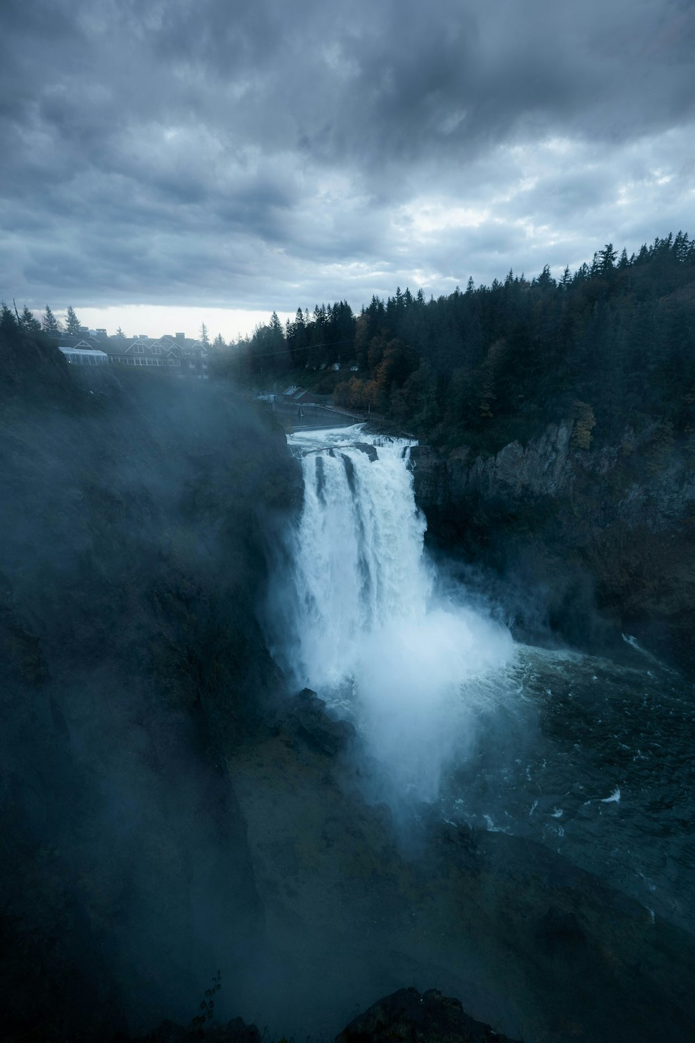 green trees near waterfalls under cloudy sky during daytime