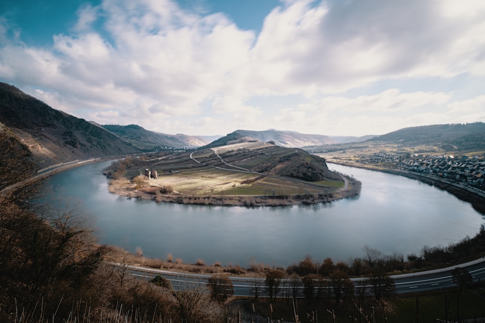 lake near mountain under white clouds and blue sky during daytime