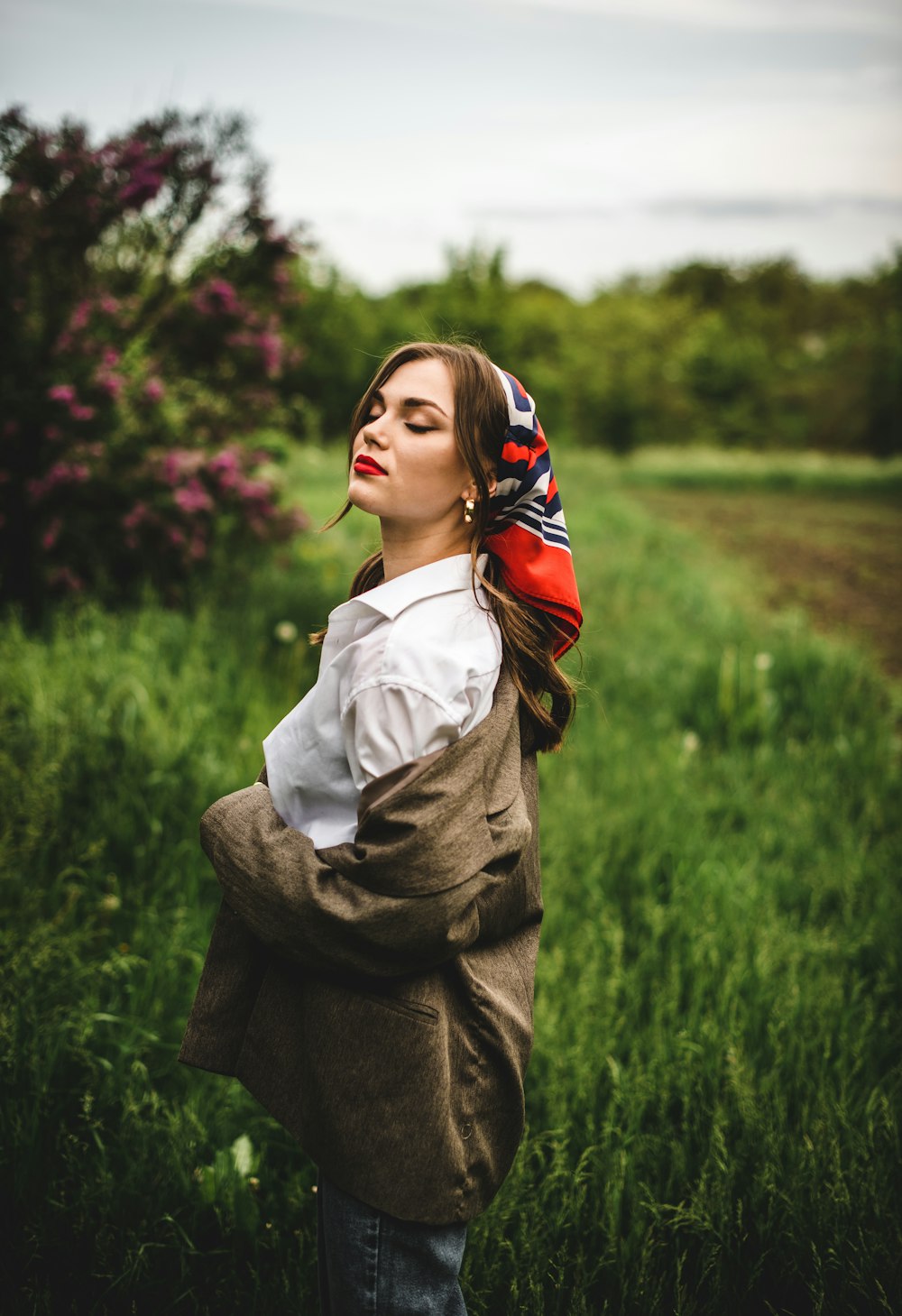 woman in white long sleeve shirt and brown coat standing on green grass field during daytime