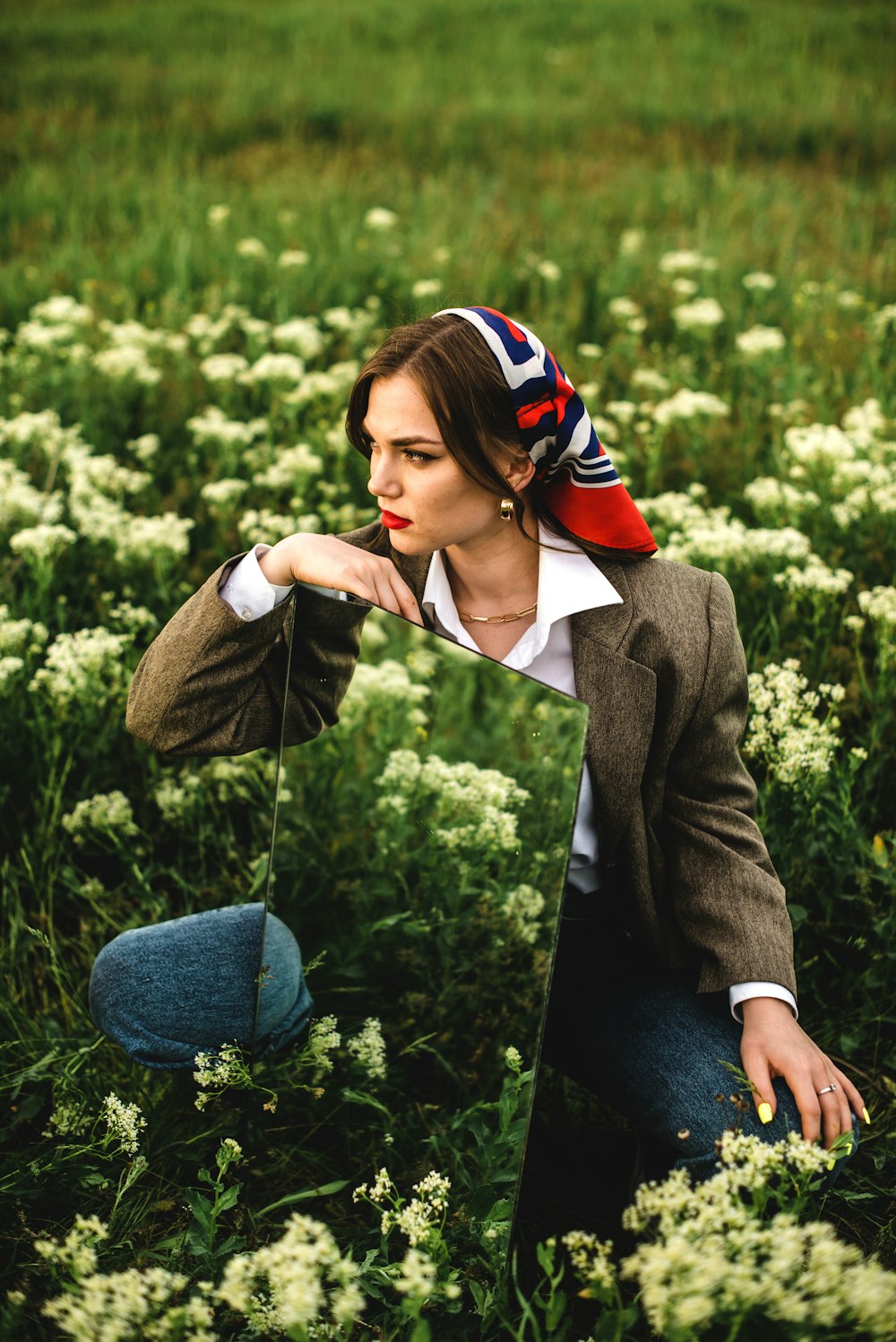 woman in black blazer and blue denim jeans sitting on green grass during daytime