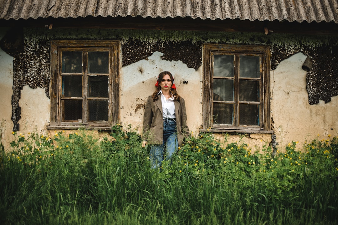 woman in white long sleeve shirt standing beside brown wooden house during daytime