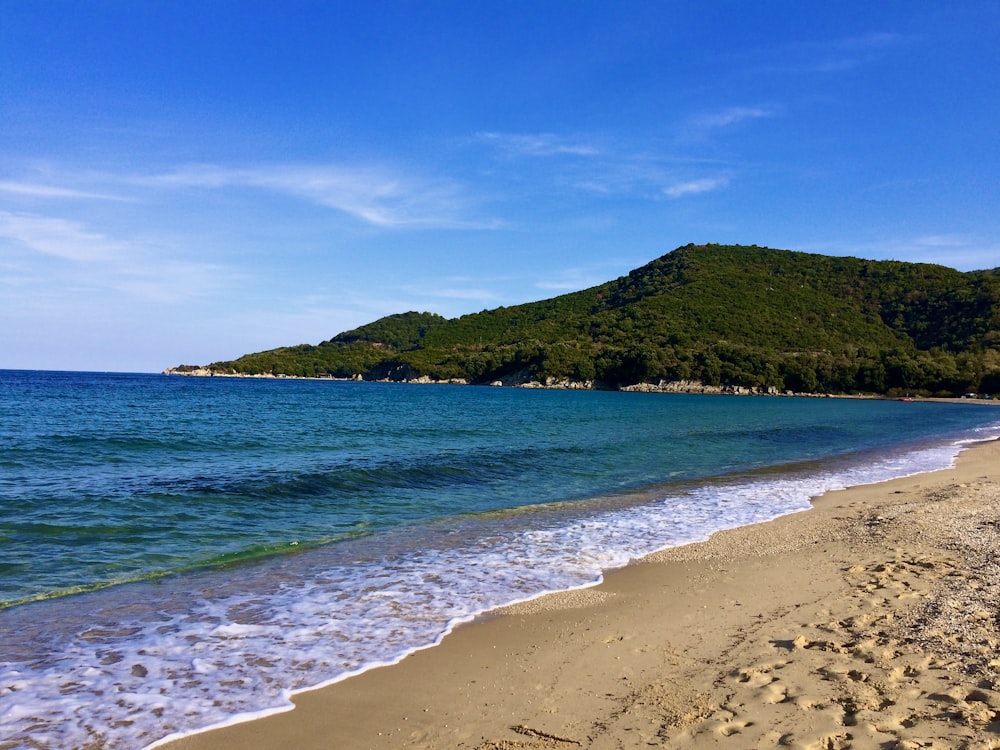 green mountain beside body of water during daytime