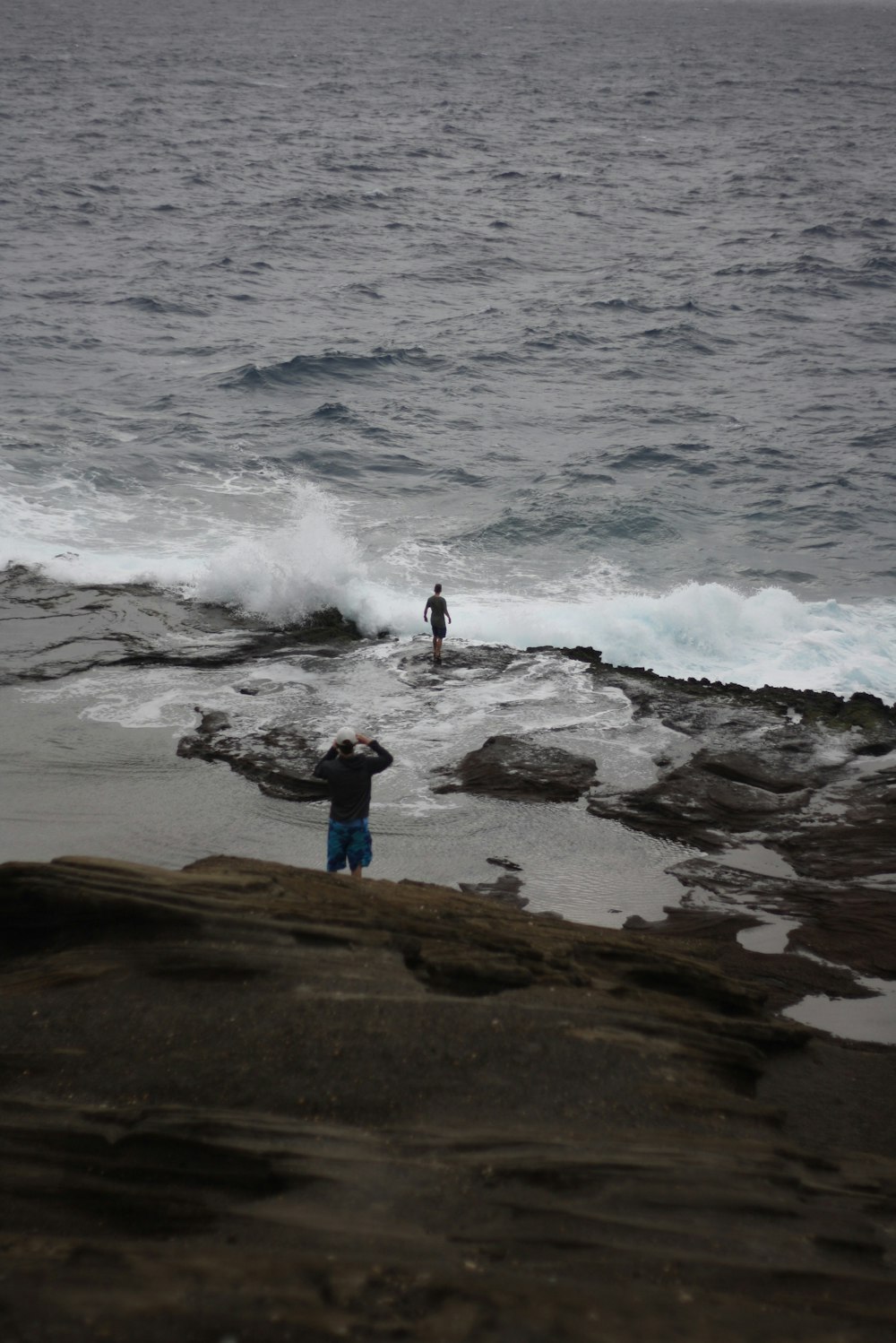 person in blue shirt standing on brown rock near sea waves during daytime