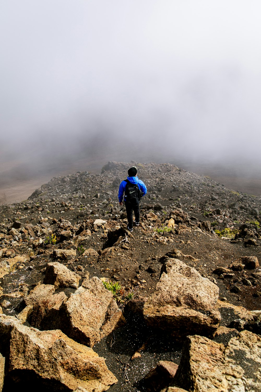 person in blue jacket walking on rocky hill