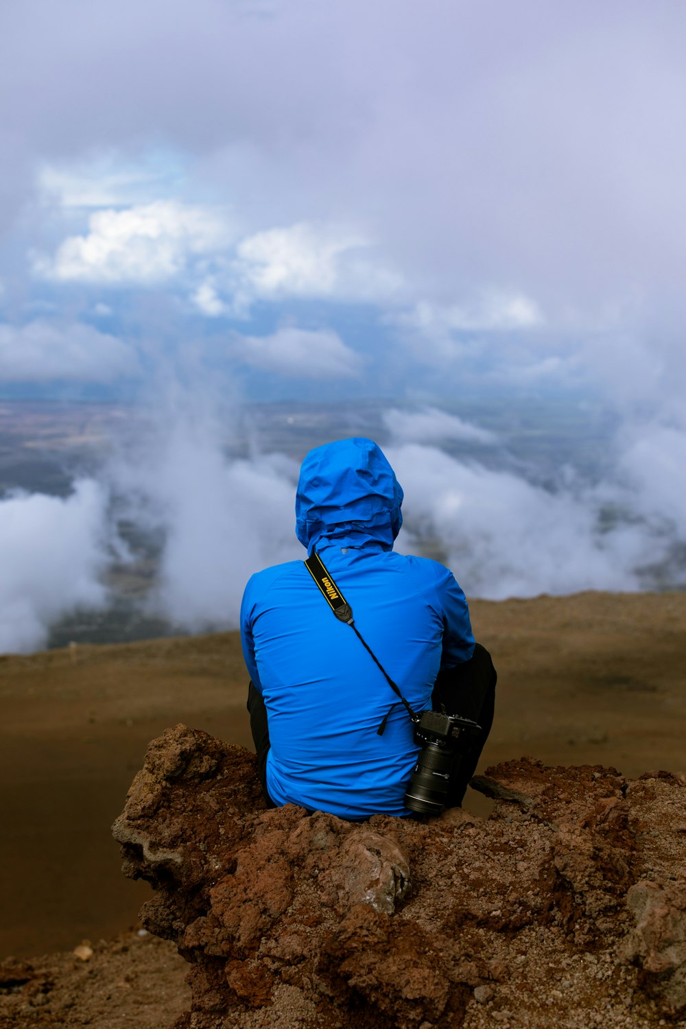 person in blue hoodie and black backpack standing on brown rock