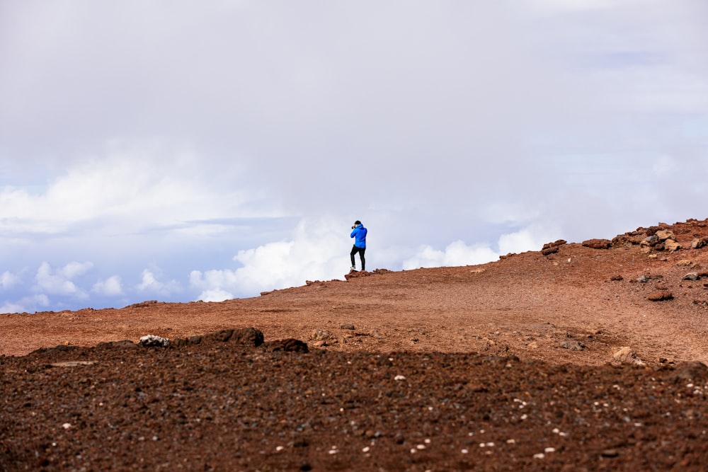 person in blue jacket walking on brown sand under white cloudy sky during daytime