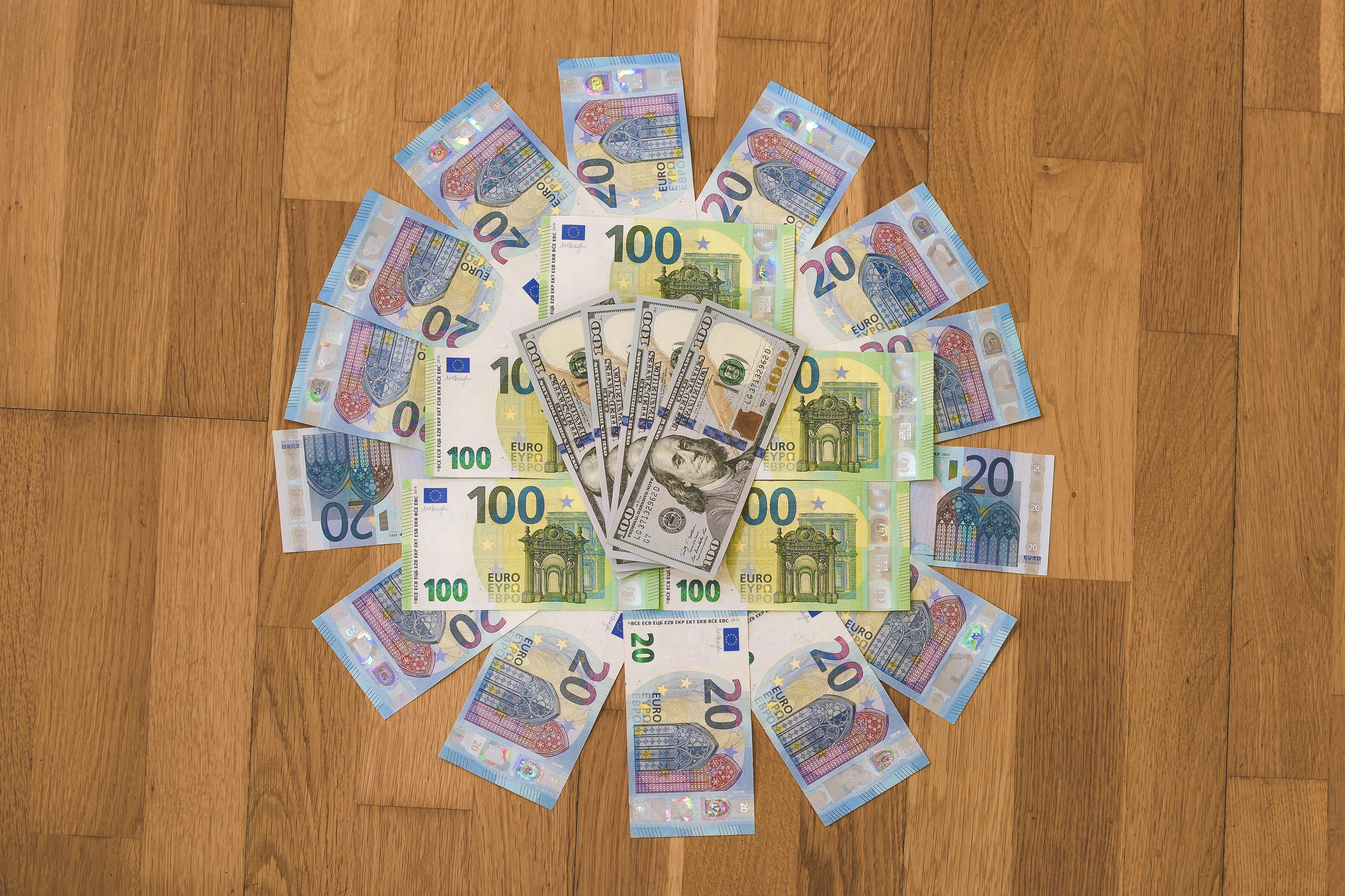 20, 100 Euro (EUR), and 100 Dollar (USD) banknotes placed on a wooden surface in a circular shape.