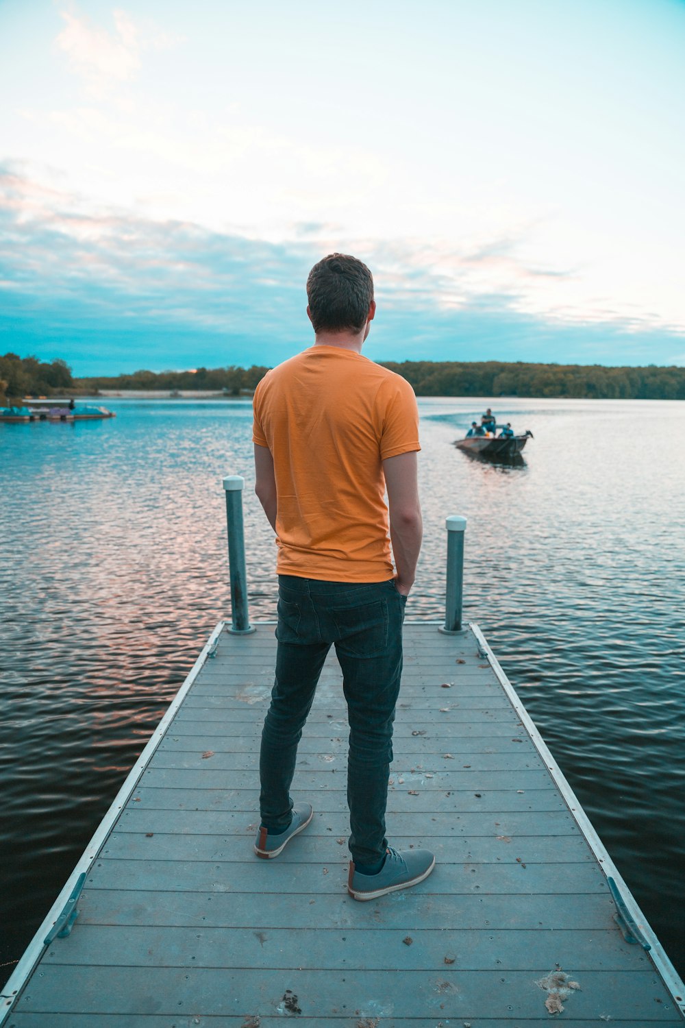 man in white shirt and black pants standing on dock during daytime
