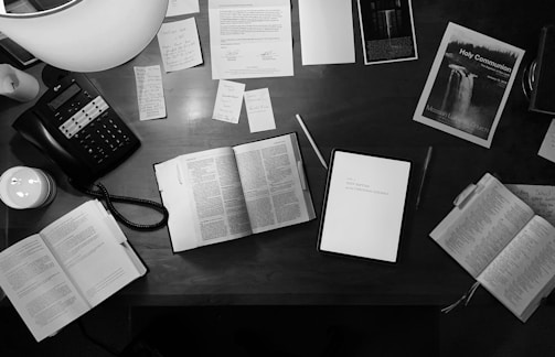 Books and digital devices on a wooden desk for learning.