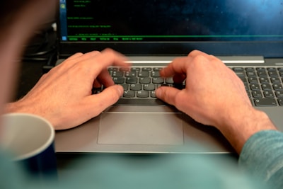 A close-up of hands typing on a laptop with a coffee cup nearby.