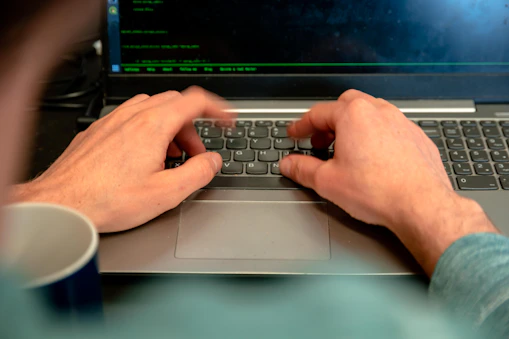 Close-up of hands typing on a laptop surrounded by research notes and a coffee cup.