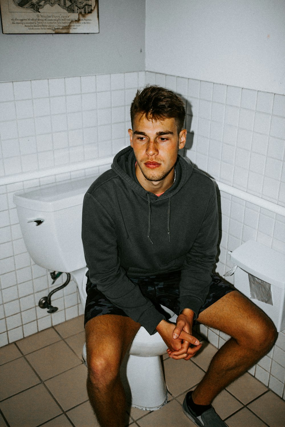 man in black hoodie sitting on toilet bowl