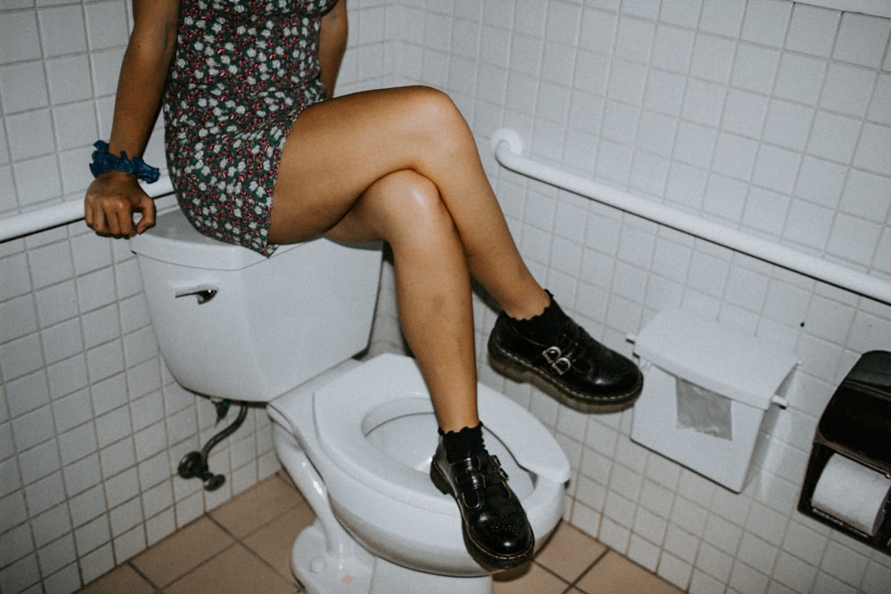 woman in black and white floral dress sitting on white ceramic toilet bowl