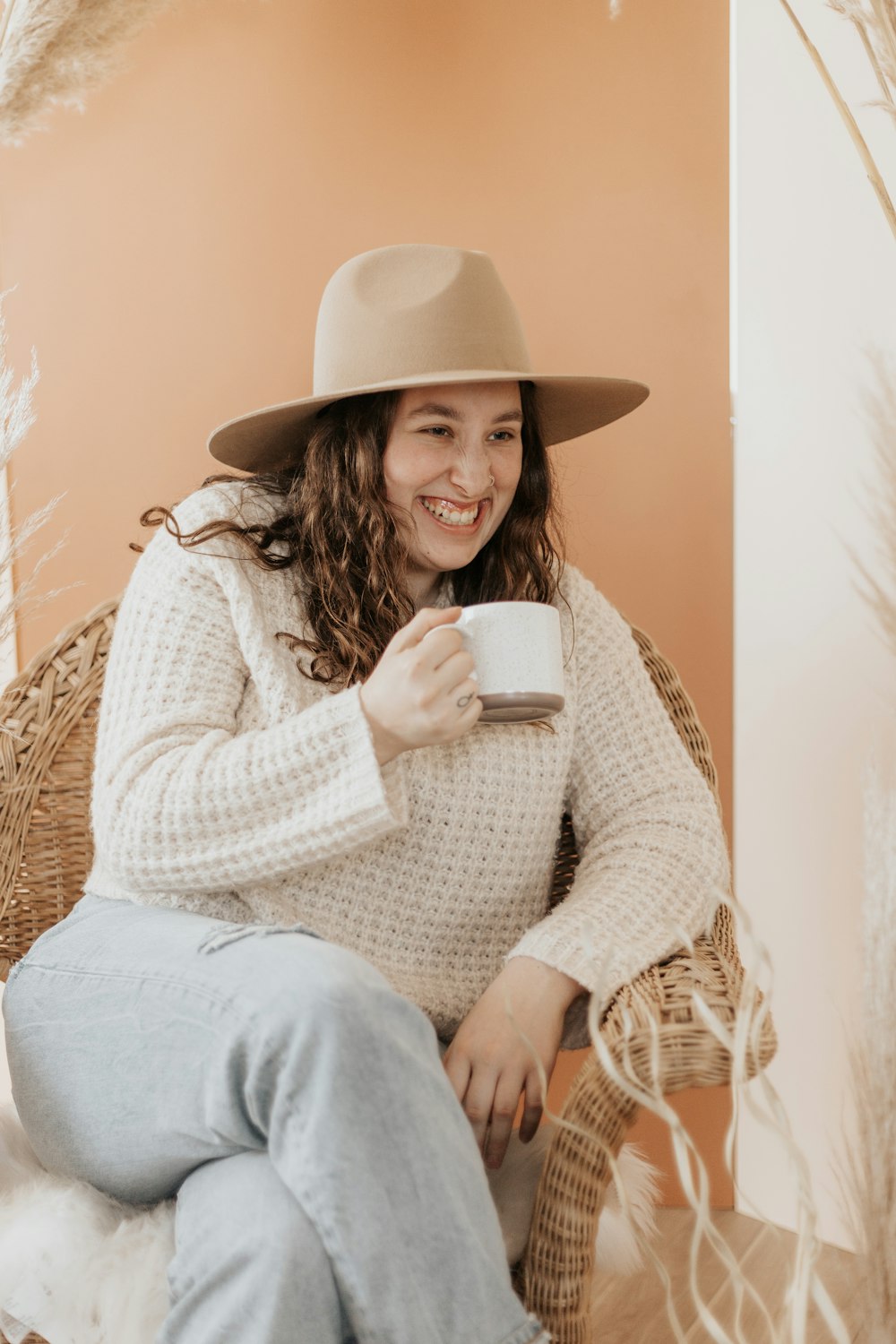 woman in white knit sweater and gray pants holding white ceramic mug