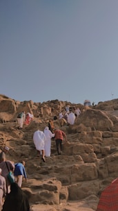 A group climbing a rocky mountain path under a clear blue sky.