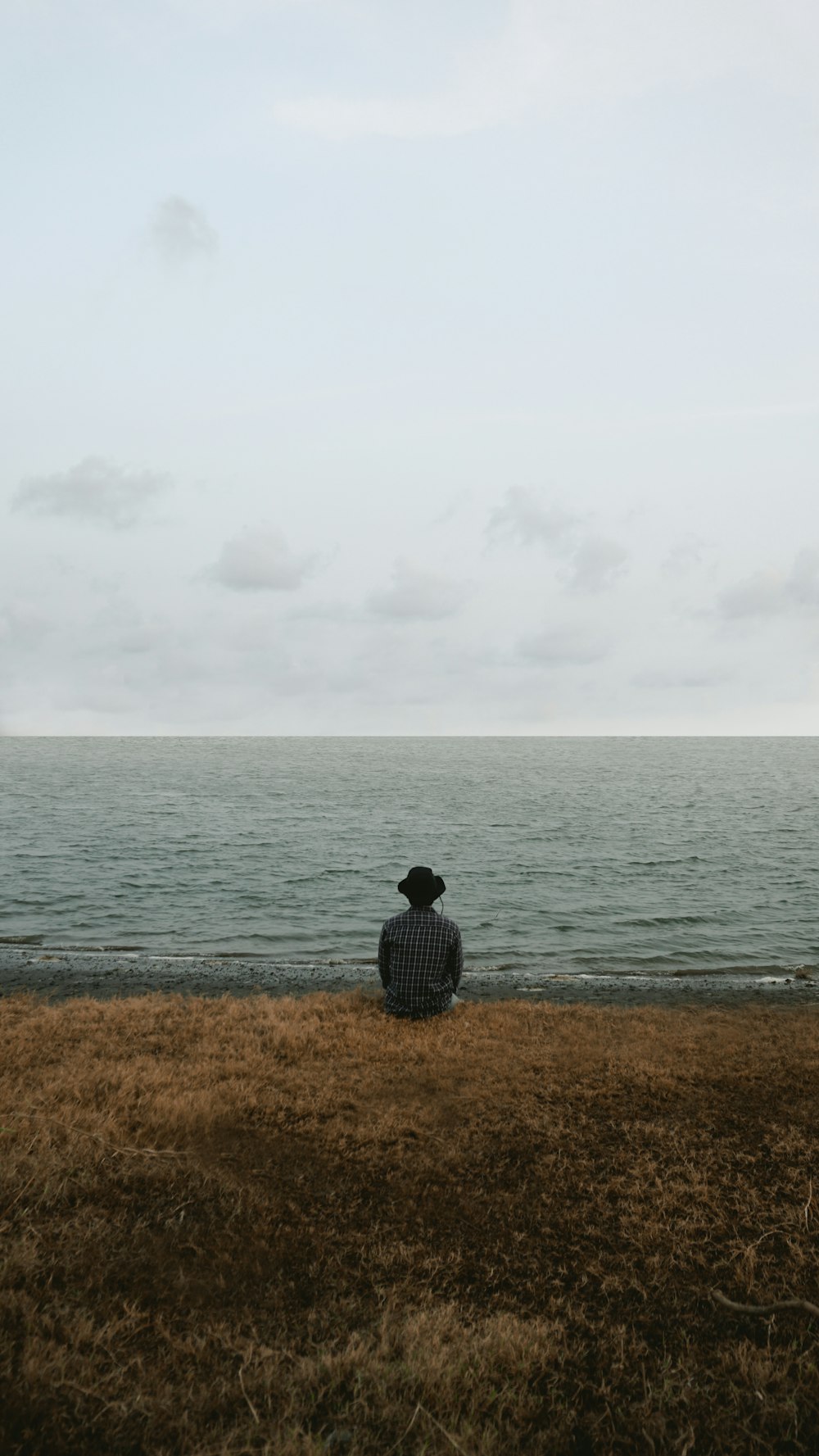 man in black and white checkered dress shirt sitting on brown grass field near body of near near near near