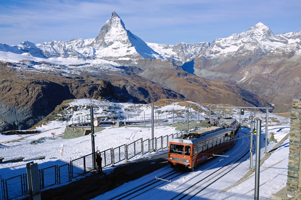 rot-schwarzer Zug auf der Schiene in der Nähe des schneebedeckten Berges tagsüber