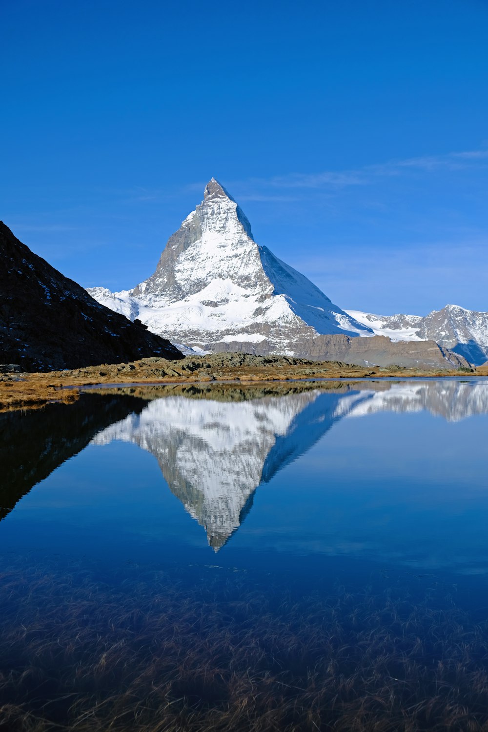 snow covered mountain near lake under blue sky during daytime