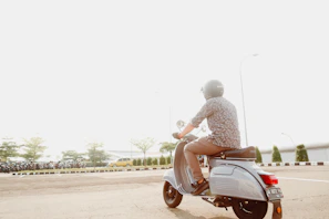 A rider on a scooter cruising through a vibrant Thai village street under bright sunlight.