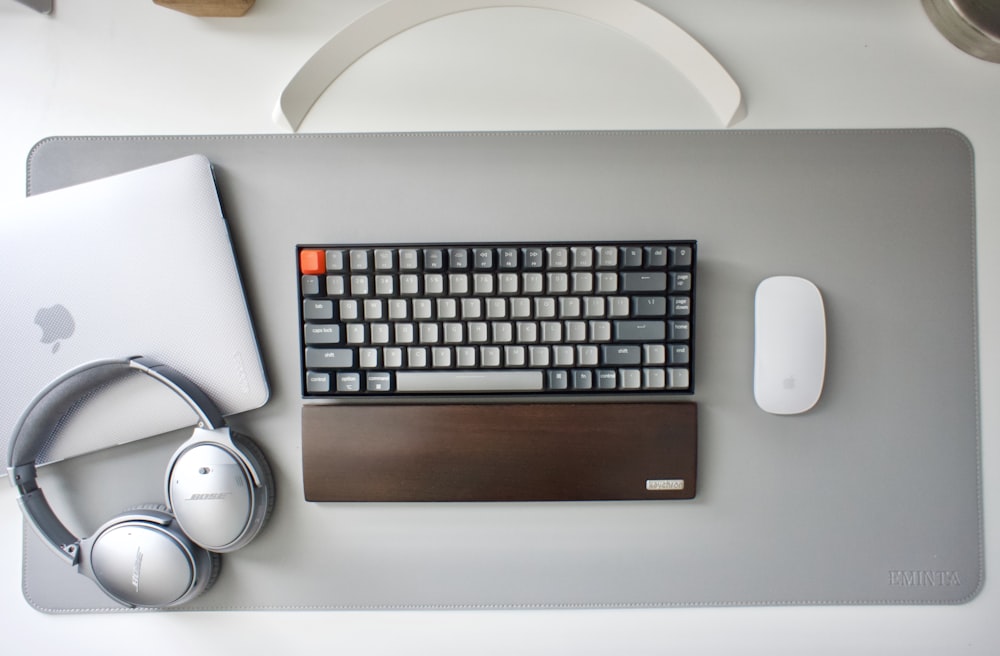 silver apple keyboard beside white and black headphones
