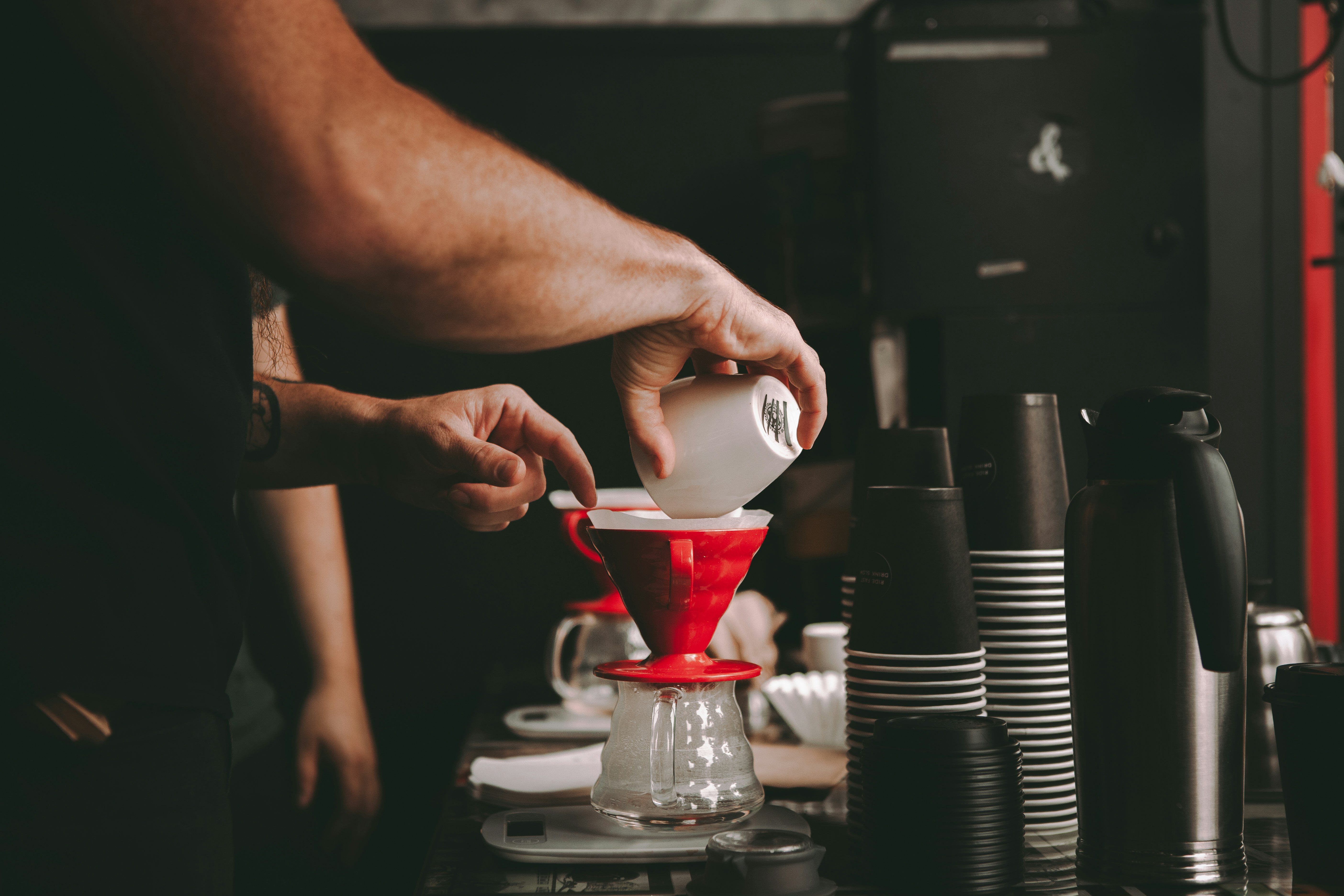 person pouring red liquid on white ceramic teacup