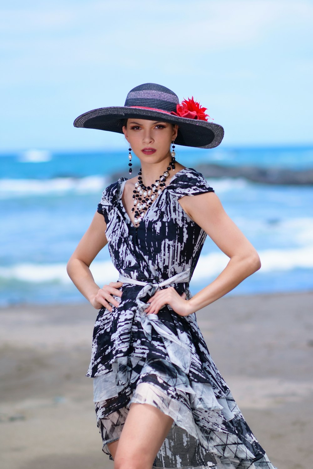 woman in black and white floral dress wearing red sun hat standing on beach during daytime