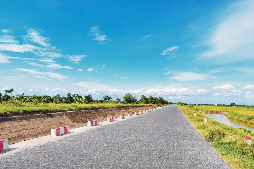 gray concrete pathway between green grass field under blue sky during daytime