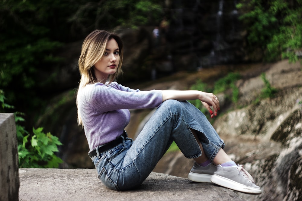 donna in maglione bianco e jeans blu denim seduta su panchina di cemento durante il giorno