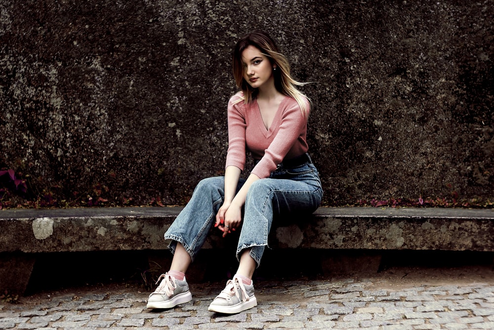 mulher na camisa rosa de manga comprida e jeans jeans azul sentada no banco de concreto